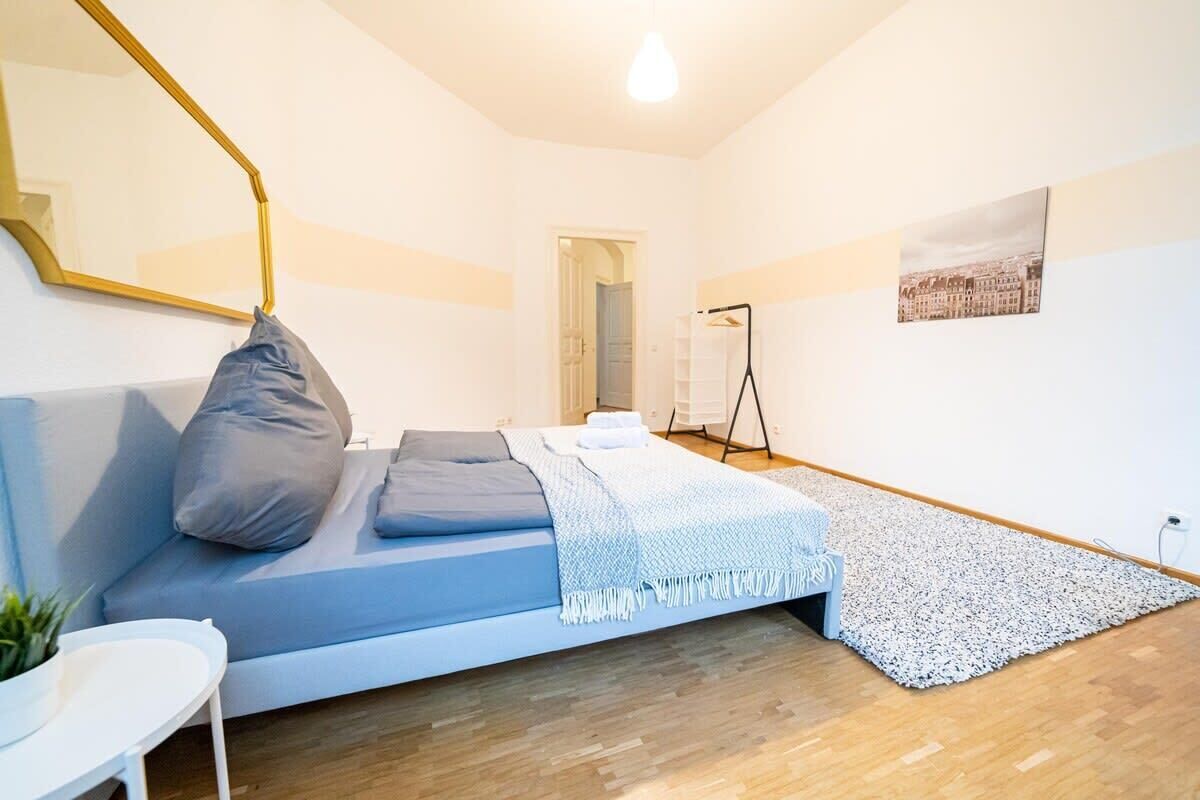 Ein modernes Schlafzimmer mit Bett, Spiegel, kleinem Tisch und Blick auf die Stadt durch ein Fenster.