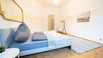Ein modernes Schlafzimmer mit Bett, Spiegel, kleinem Tisch und Blick auf die Stadt durch ein Fenster.