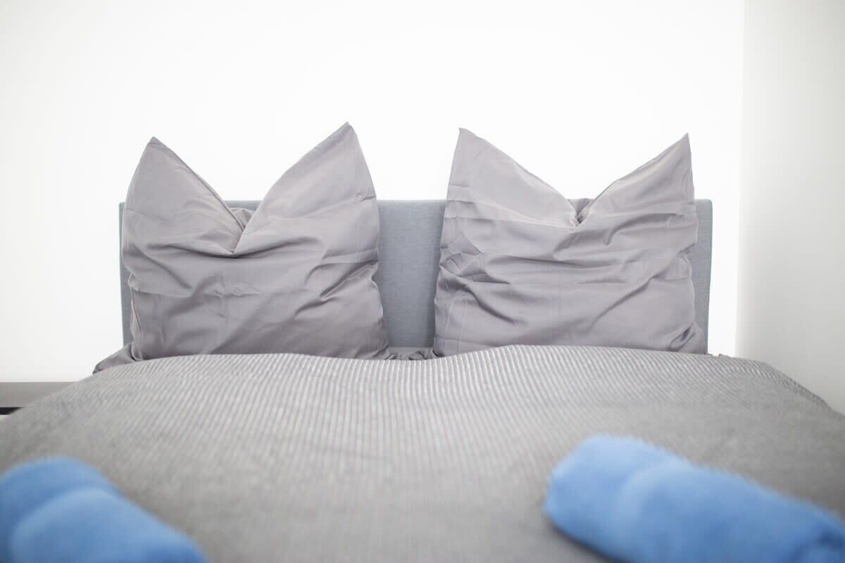 A bed with grey bedding and pillows, and a blue blanket partially visible.