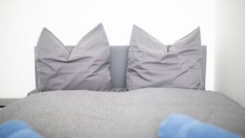 A bed with grey bedding and pillows, and a blue blanket partially visible.