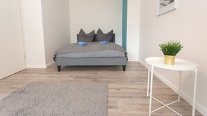 A bedroom with a bed, a small white table with a plant, and a grey rug. - FullHouse | Chemnitz | Rosenhof C8 | Zentrum (Chemnitz)