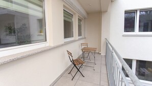 A balcony with two wooden tables and chairs, large windows, and a white exterior wall. - FullHouse | Chemnitz | Rosenhof C8 | Zentrum (Chemnitz)
