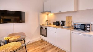 A compact kitchen with white cabinets, a built-in oven, a microwave, and a coffee maker. There is a glass table with woven placemats and a chair. - FullHouse Premium Apt. H11 (Leipzig)