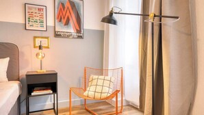 A modern bedroom with a bed, a nightstand with a lamp, a metal-framed chair, and a poster on the wall. - FullHouse Premium Apt. H11 (Leipzig)