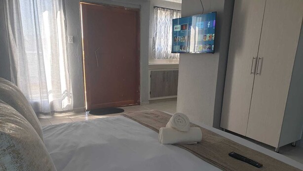 A hotel room with a bed, a TV mounted on the wall, a wardrobe, and a door. - Tsamatiku Guesthouse (Mangwazi)