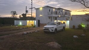 A white two-story house with a driveway and a white car parked in front. - Tsamatiku Guesthouse (Mangwazi)