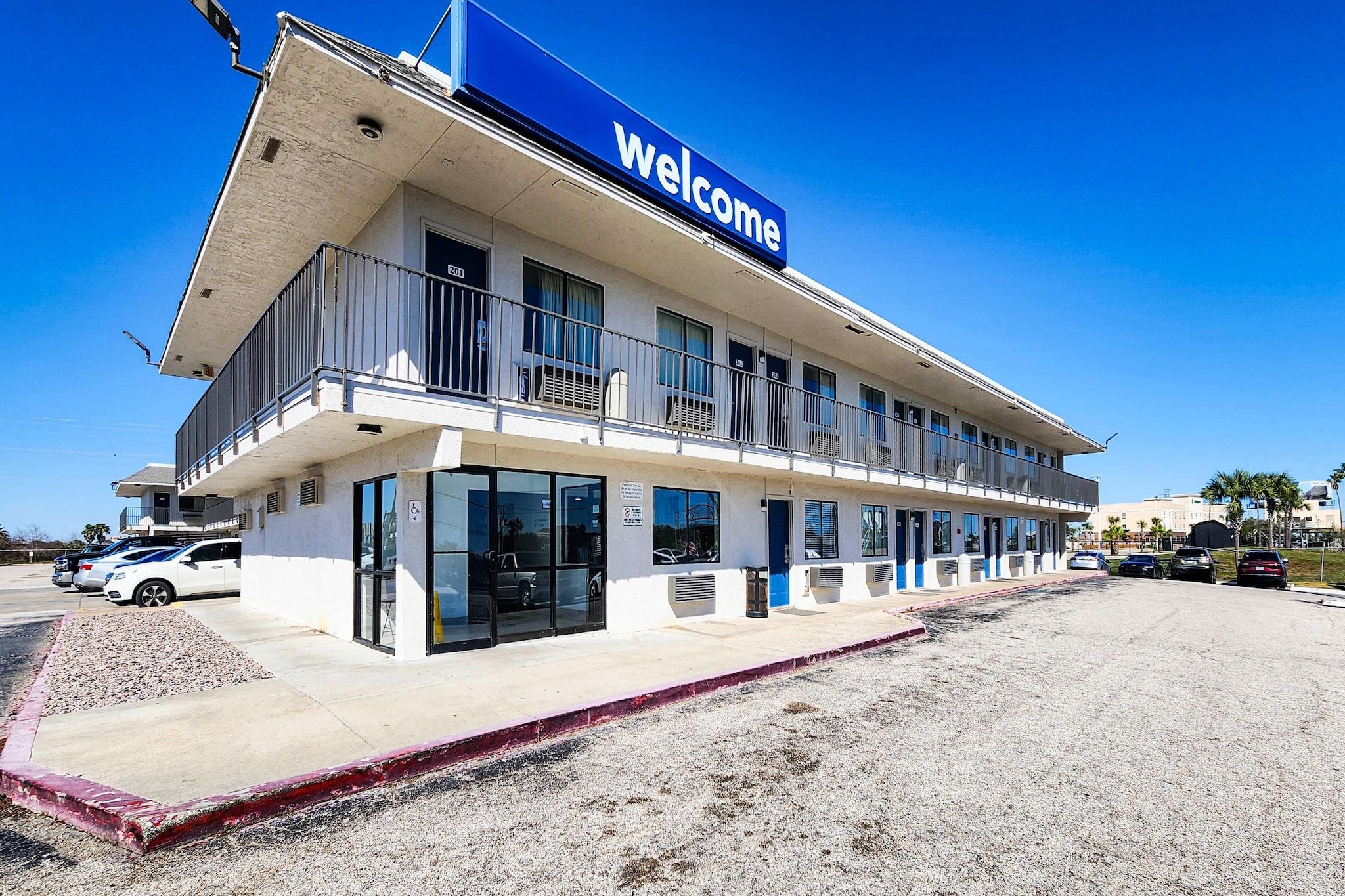 A hotel with a 'Welcome' sign, multiple balconies, and a parking lot.