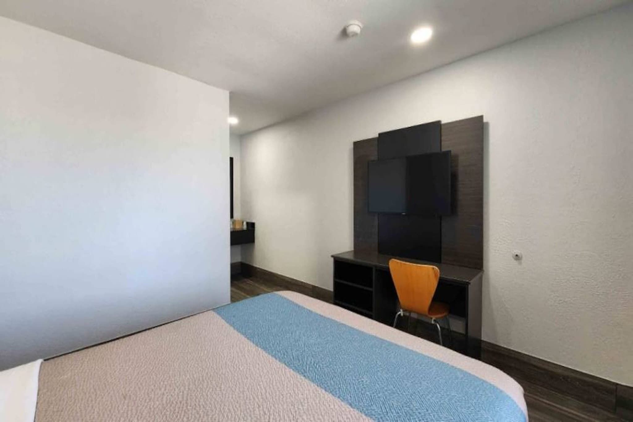 Ein Hotelzimmer mit Bett, Schreibtisch und einem an der Wand befestigten Fernseher.