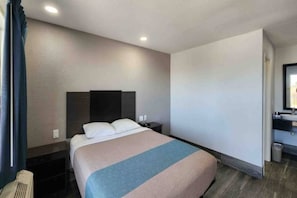 Quarto de hotel com cama, mesa de cabeceira, espelho e banheiro.