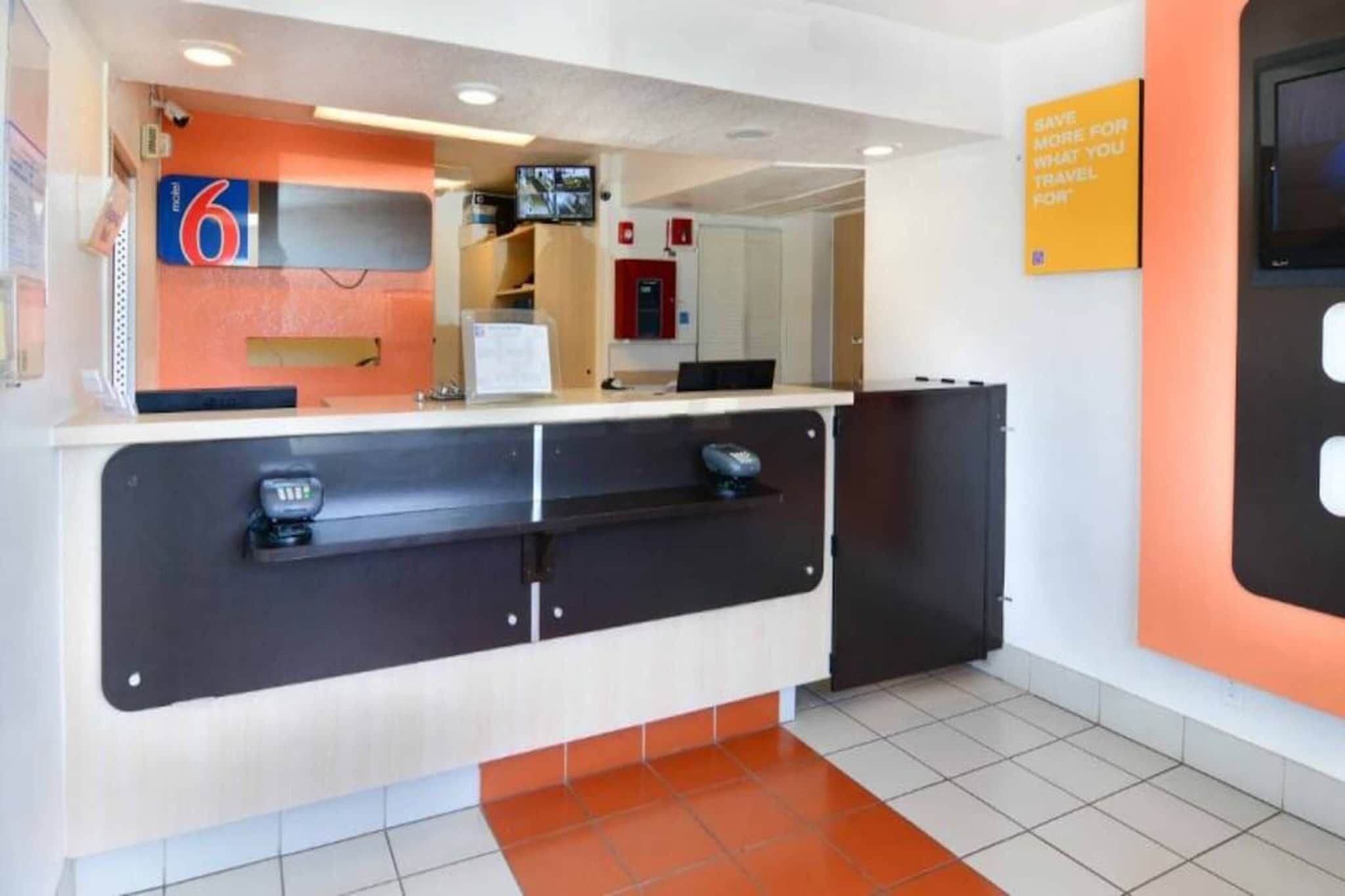 A hotel reception desk with a digital screen, a counter, and a sign about saving for travel.