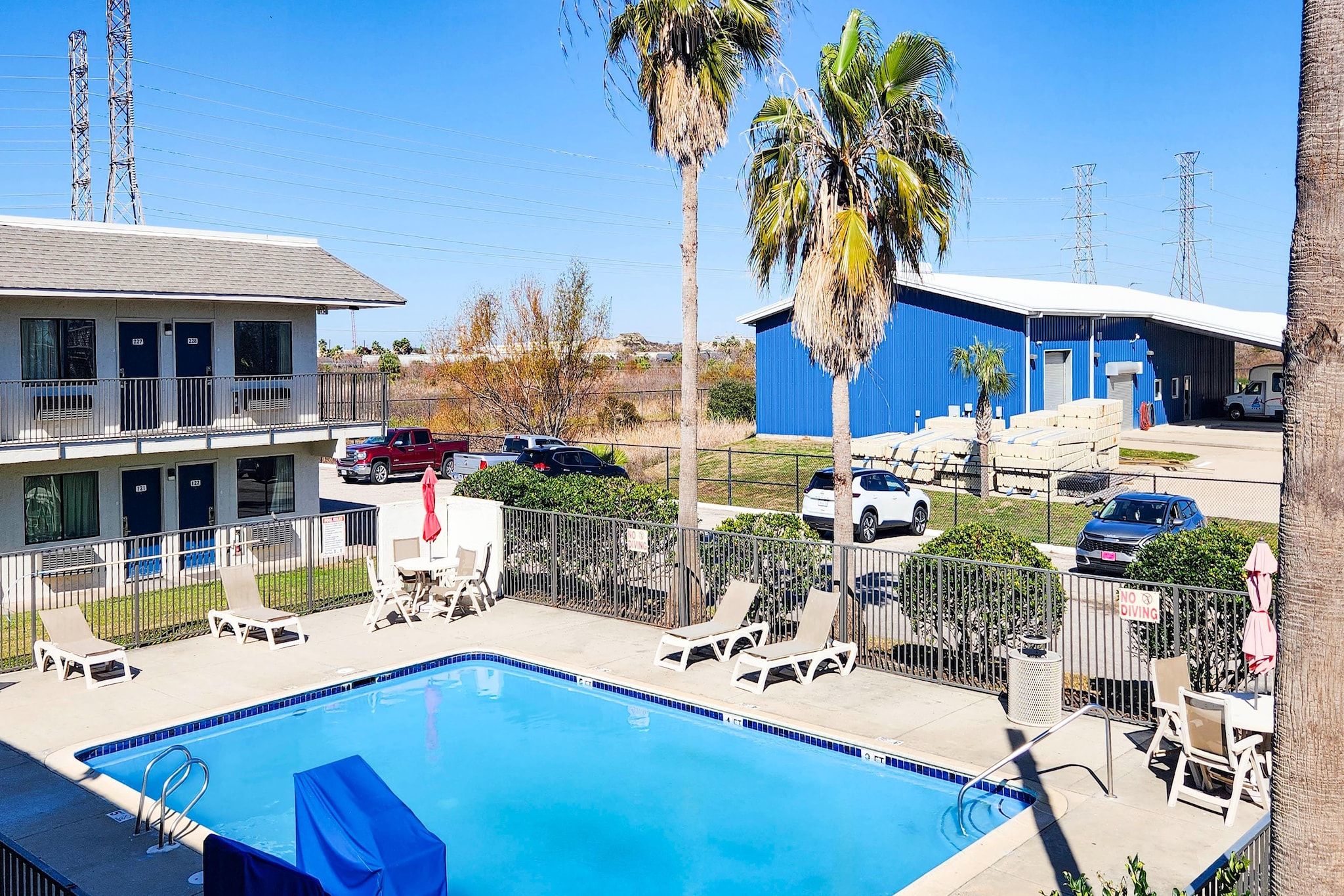Piscina com espreguiçadeiras, área coberta e edifício com fachada azul.