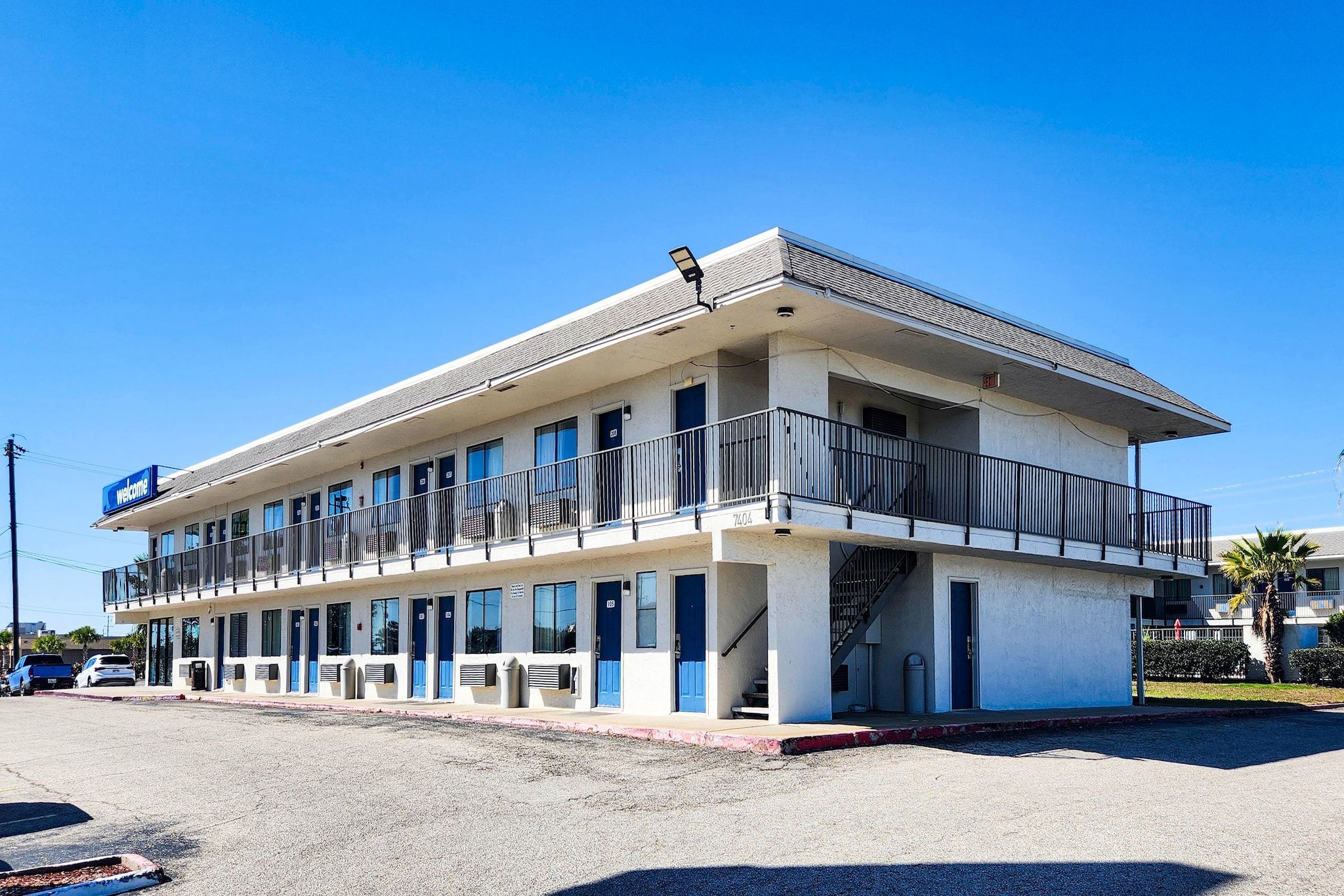 A two-story motel with a flat roof, multiple balconies, and a 'Welcome' sign.