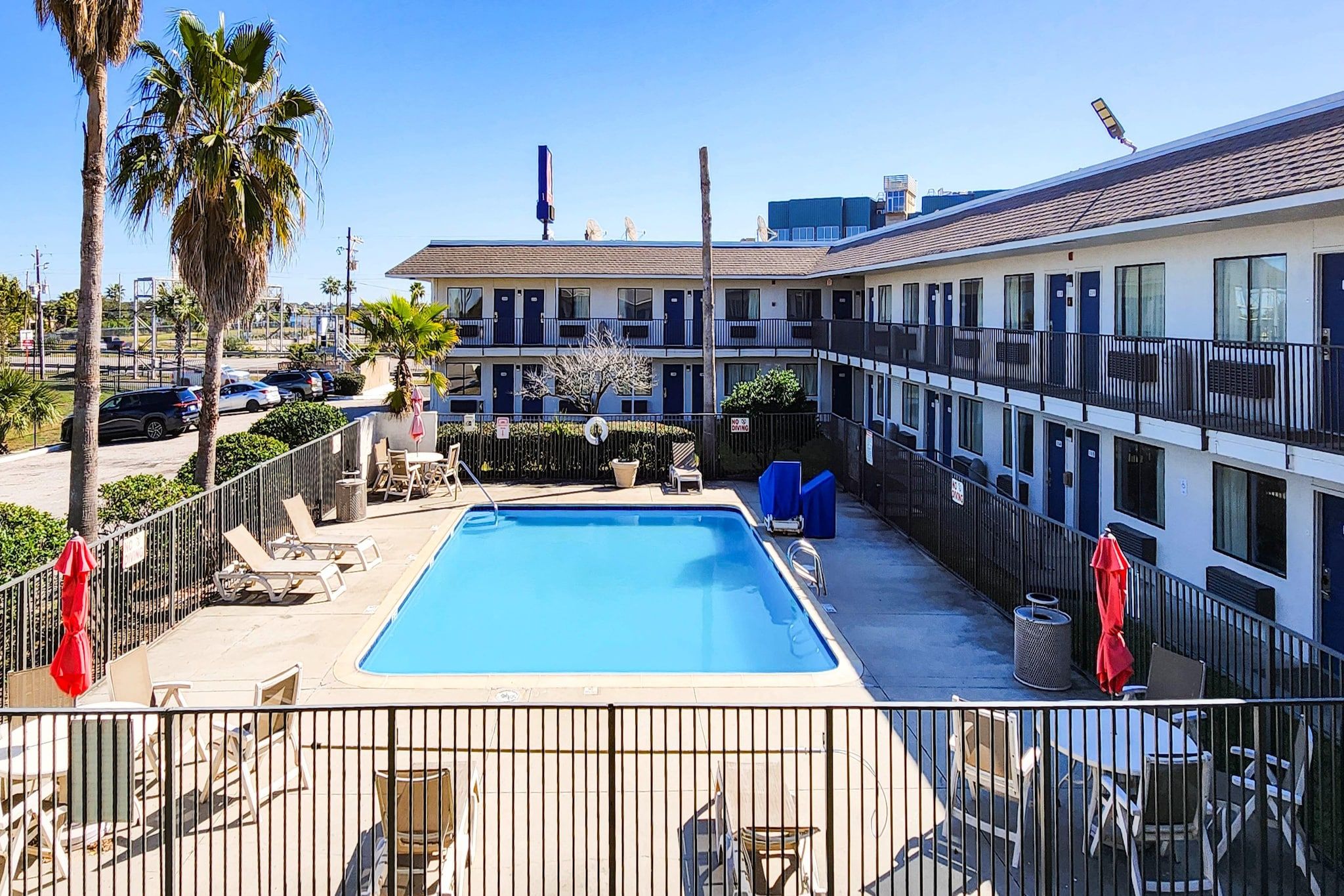 A pool area with lounge chairs and umbrellas, surrounded by a fence, with a building in the background.