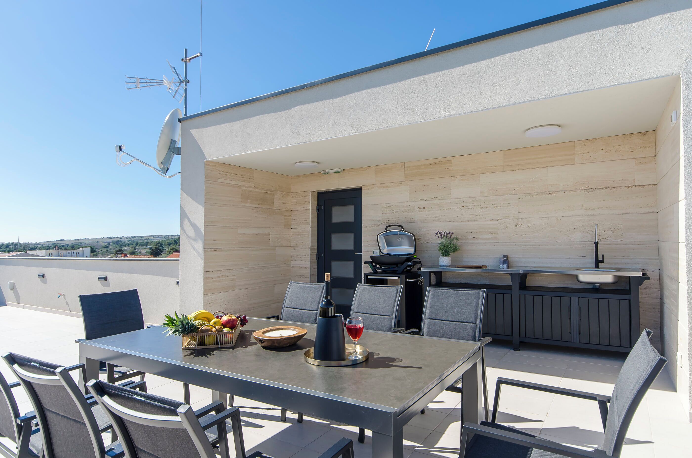 A rooftop patio with a dining table, chairs, a grill, and a small kitchen area.