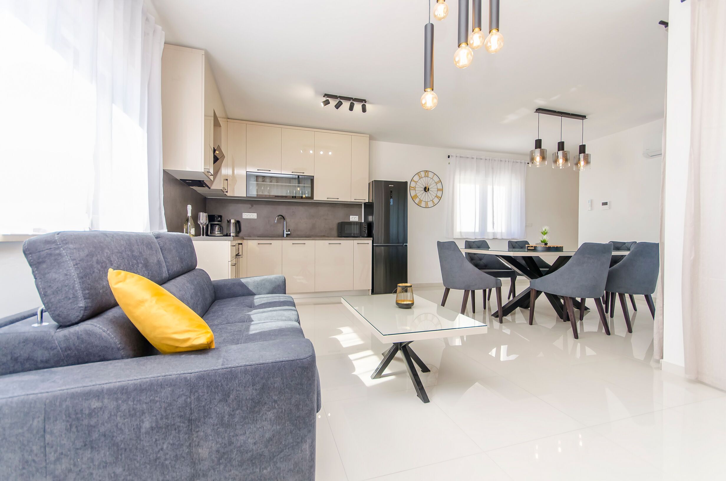 A modern living room with a grey sofa, a glass coffee table, and a dining area with a table and chairs.
