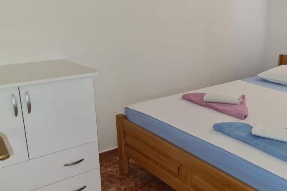 A bedroom with a wooden bed, white bedding, and a white wardrobe with drawers.