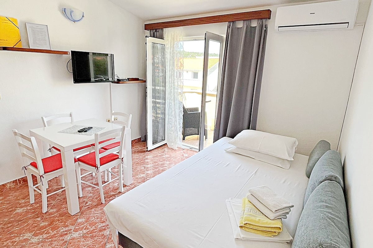 A hotel room with a bed, a desk with chairs, a television, and a sliding glass door leading to an outdoor area.