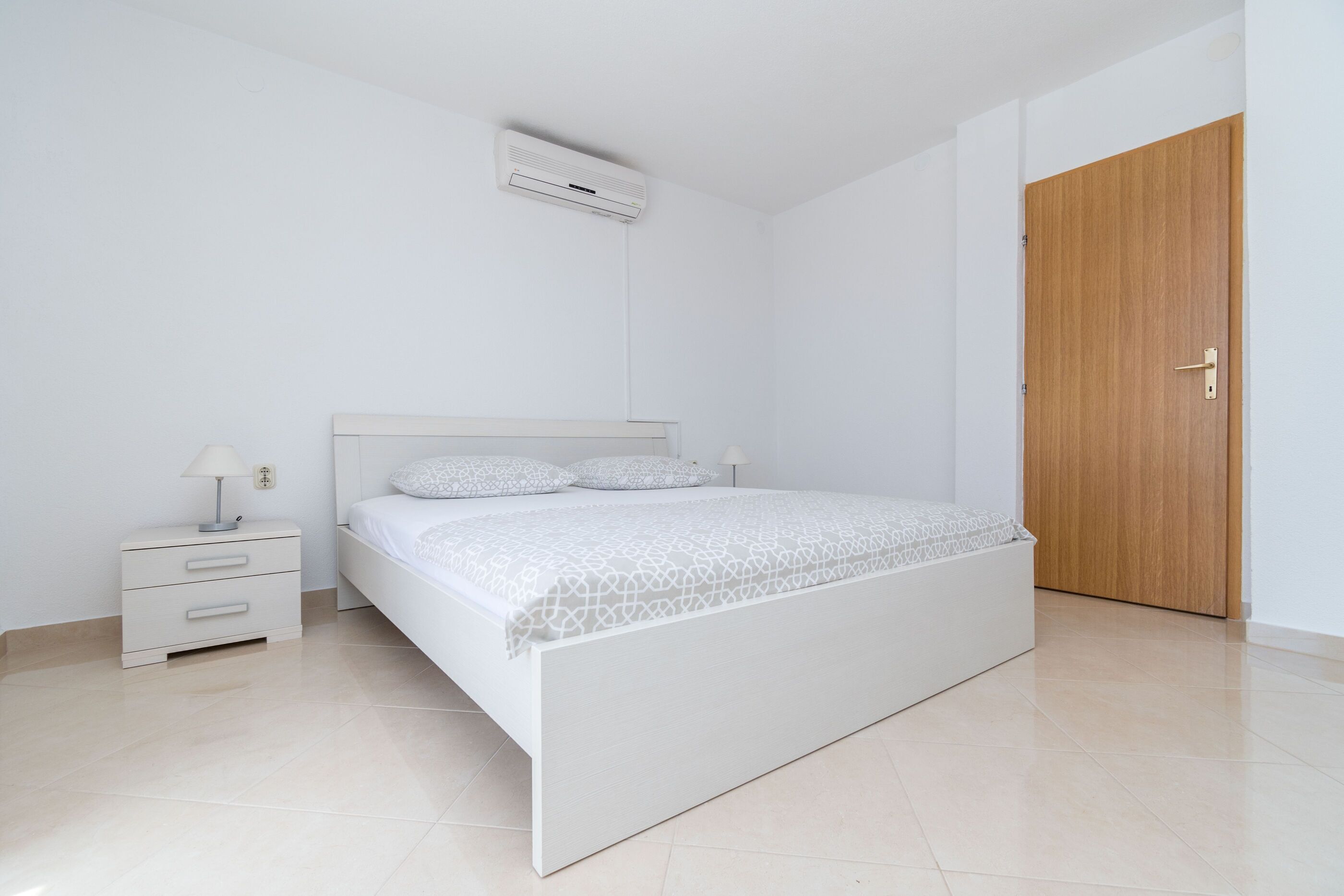 Un dormitorio minimalista con cama, mesita de noche, lámpara y una puerta de madera.