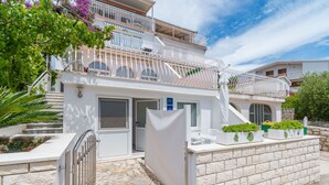 A two-story building with a white exterior, a balcony with white railings, and a stone pathway leading to the entrance. - Apartments Teresa (Seget)