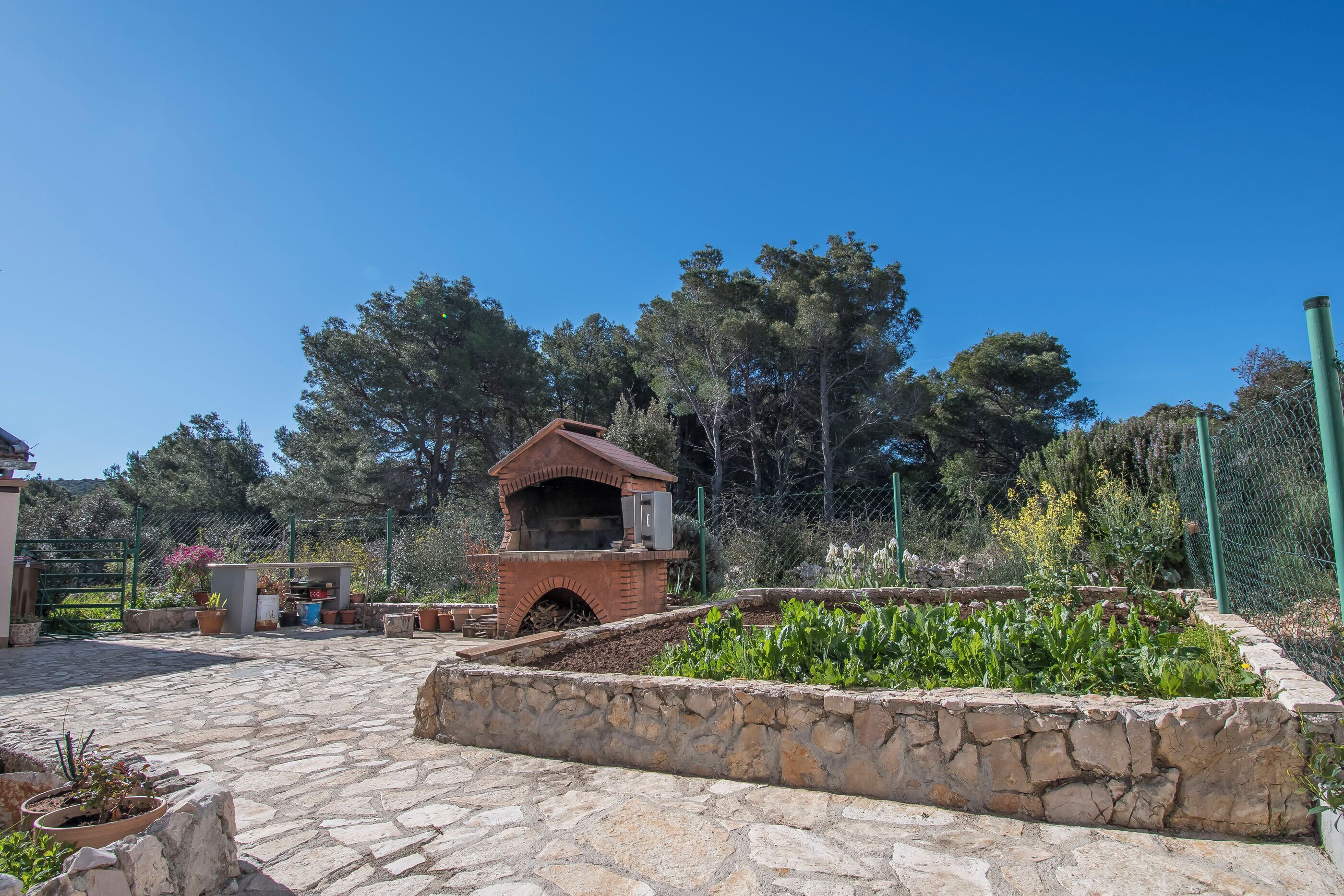 A stone patio with a brick oven, surrounded by potted plants and a stone wall.