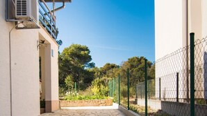 A stone-paved pathway leading to a building with a metal fence and greenery in the background. - Apartment Marasovic (Pirovac)