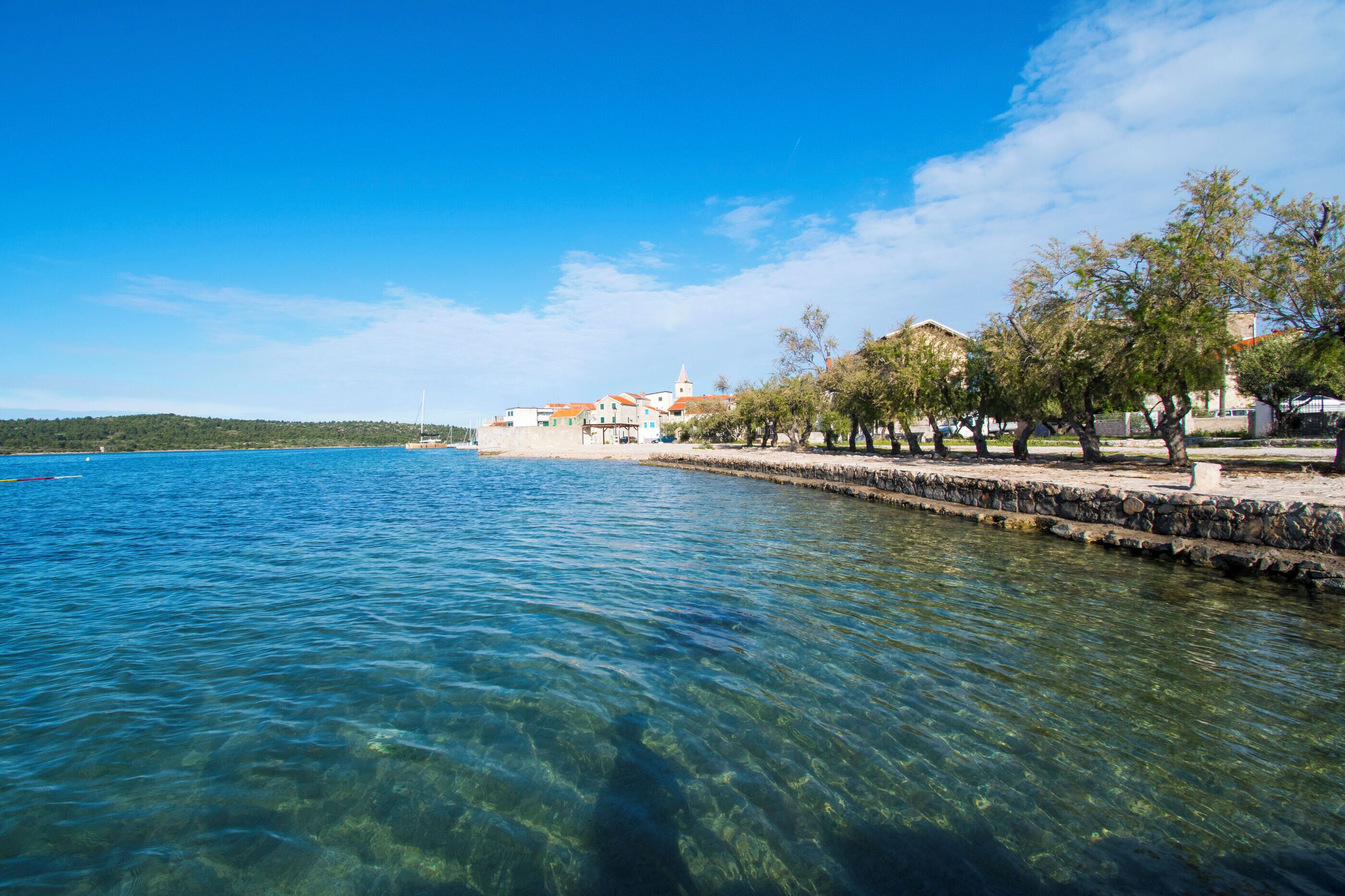 Une vue sur le front de mer, avec une eau claire, une promenade bordée de pierres et des bâtiments aux toits rouges.