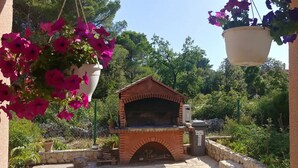 A brick-built outdoor oven with a stone base, surrounded by greenery and potted plants. - Apartment Marasovic (Pirovac)
