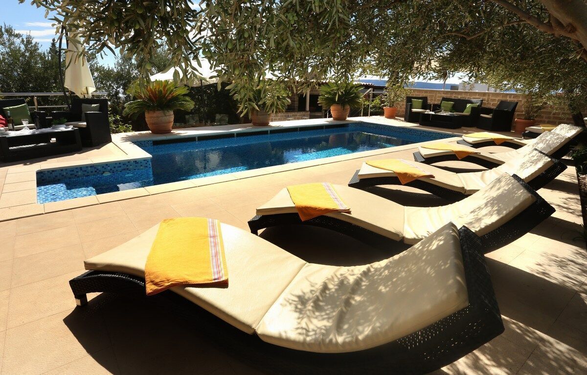 A poolside area with lounge chairs, a pool, and potted plants.