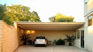 A covered parking area with a brick wall, a parked car, and potted plants. - Apartments Hermes (Okrug)