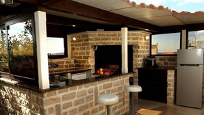 A stone-built kitchen with a built-in oven, a refrigerator, and two bar stools. - Apartments Hermes (Okrug)