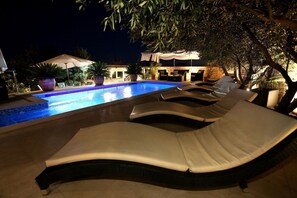 A poolside area with lounge chairs and umbrellas, surrounded by potted plants and a building in the background. - Apartments Hermes (Okrug)