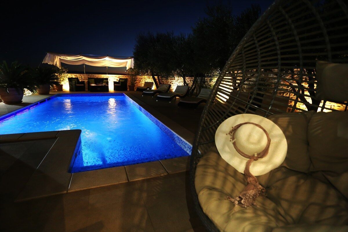 Un espace piscine nocturne doté d’un coin salon couvert et de chaises longues.