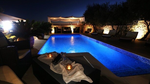 A nighttime pool area with lounge chairs and a table with candles and a phone. - Apartments Hermes (Okrug)