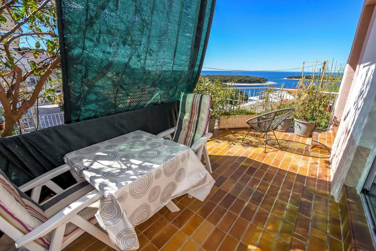 A balcony with a table and chairs, a view of the sea, and a green netting structure.