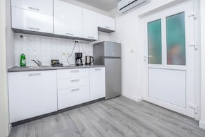 A modern kitchen with white cabinets, a stainless steel refrigerator, a coffee maker, and a dishwasher. - Apartments Aldo (Primosten)
