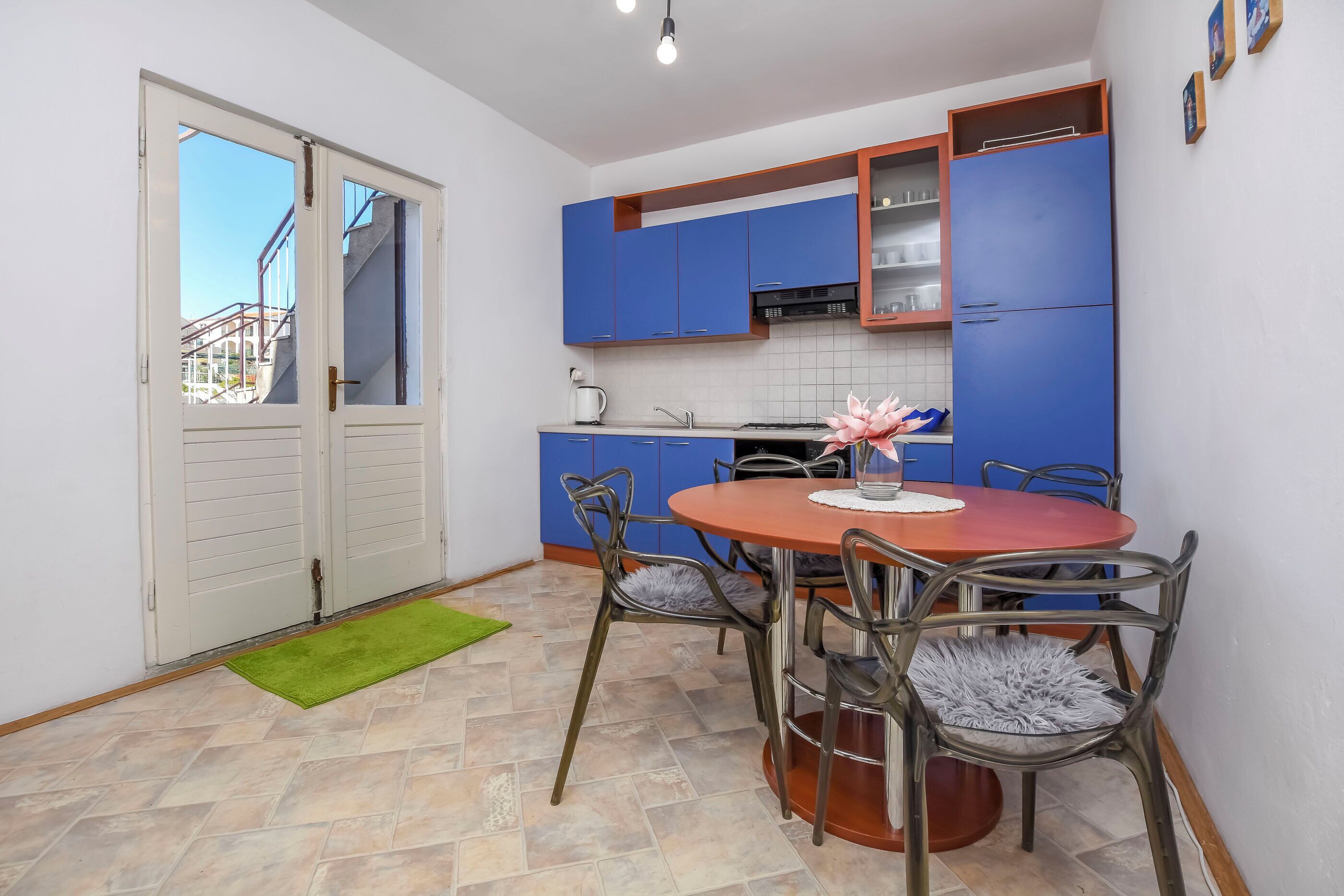 Een kleine keuken met blauwe kastjes, een ronde houten tafel en een groen vloerkleed.
