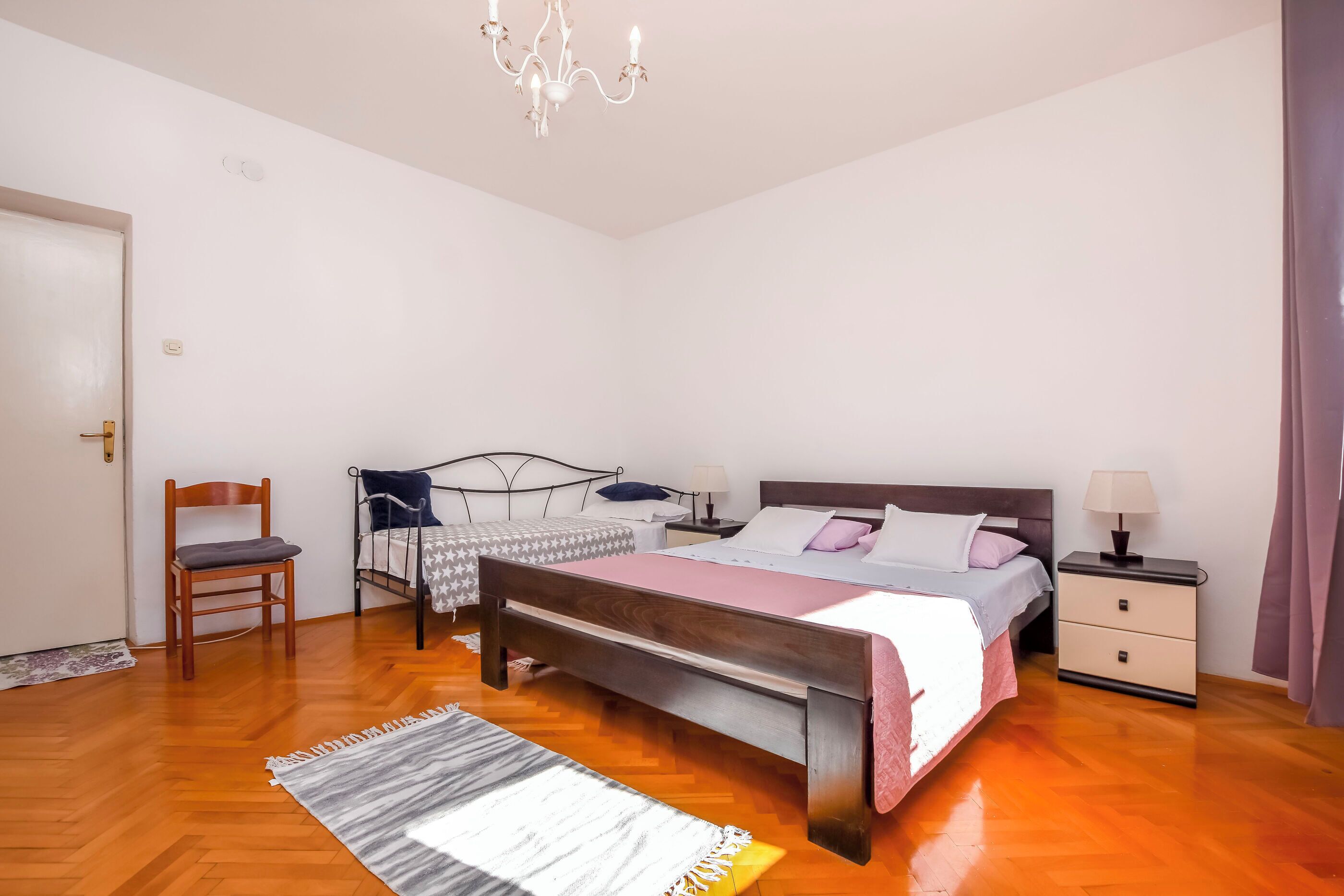 A bedroom with a wooden bed, a nightstand, a chair, and a chandelier.