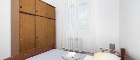 Une chambre à coucher avec une armoire en bois, un lit recouvert d’une couette à rayures grises et jaunes, et une table de chevet avec une lampe.