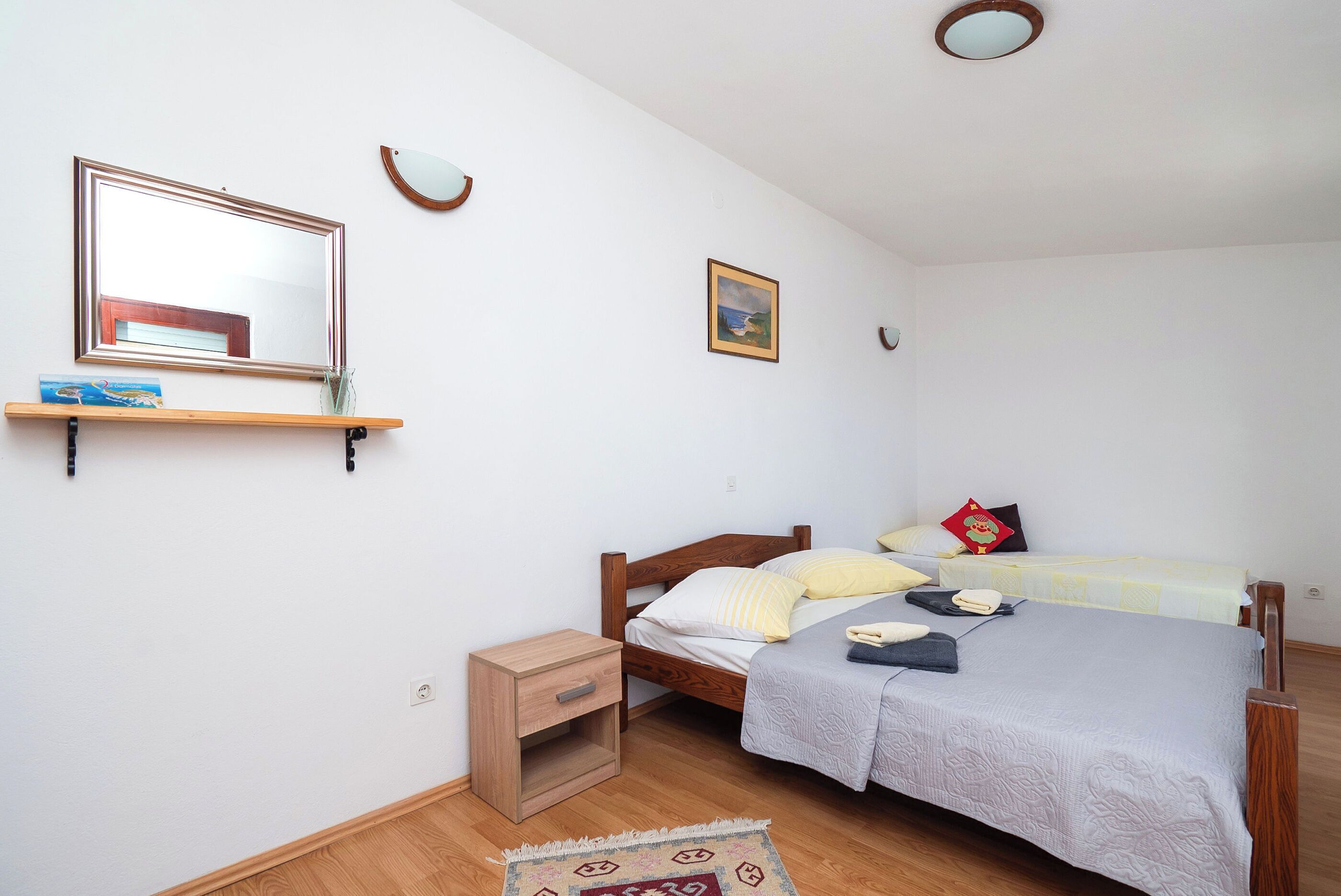 A bedroom with two beds, a nightstand, a mirror, and a shelf with a book and a vase.