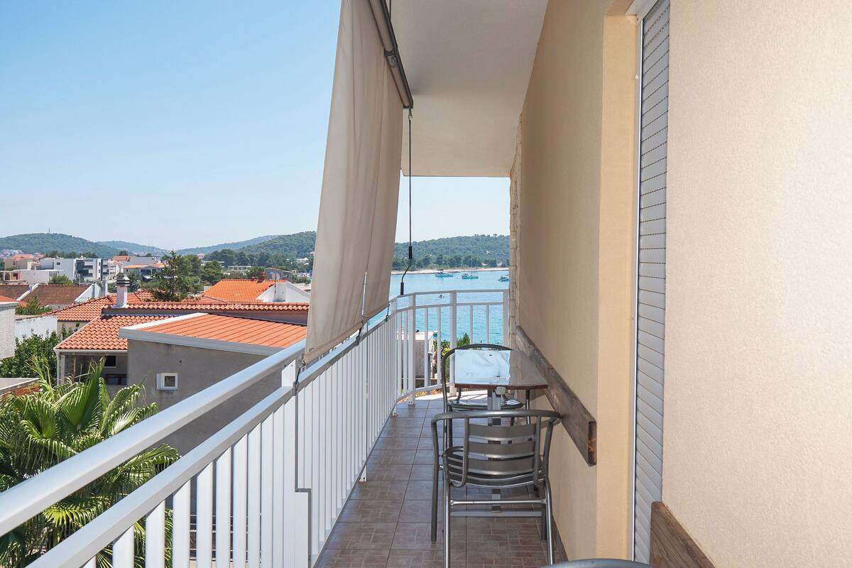 A balcony with a table and chairs, overlooking a beach and water.