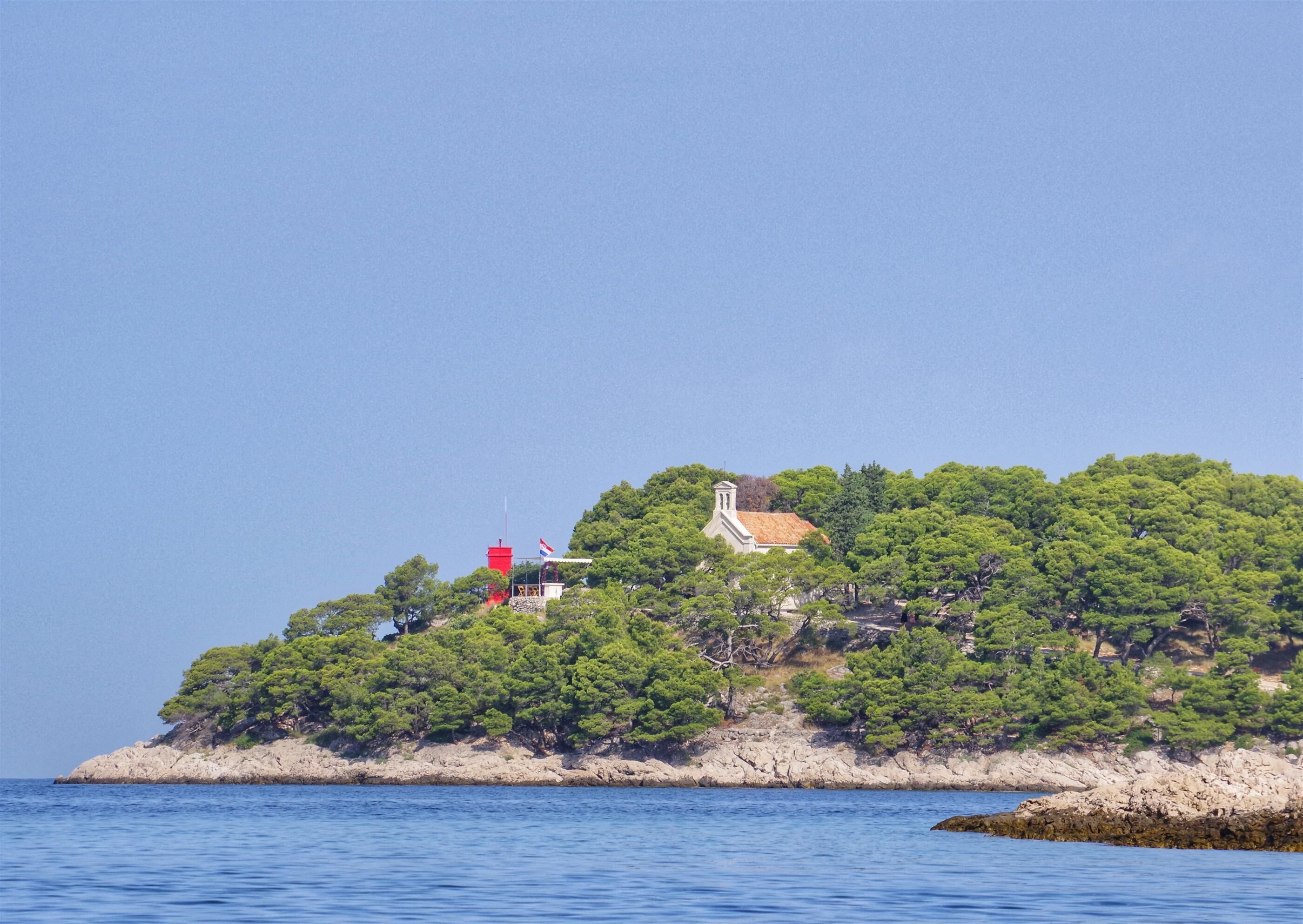 A small island with a church and a red building, surrounded by clear blue water.
