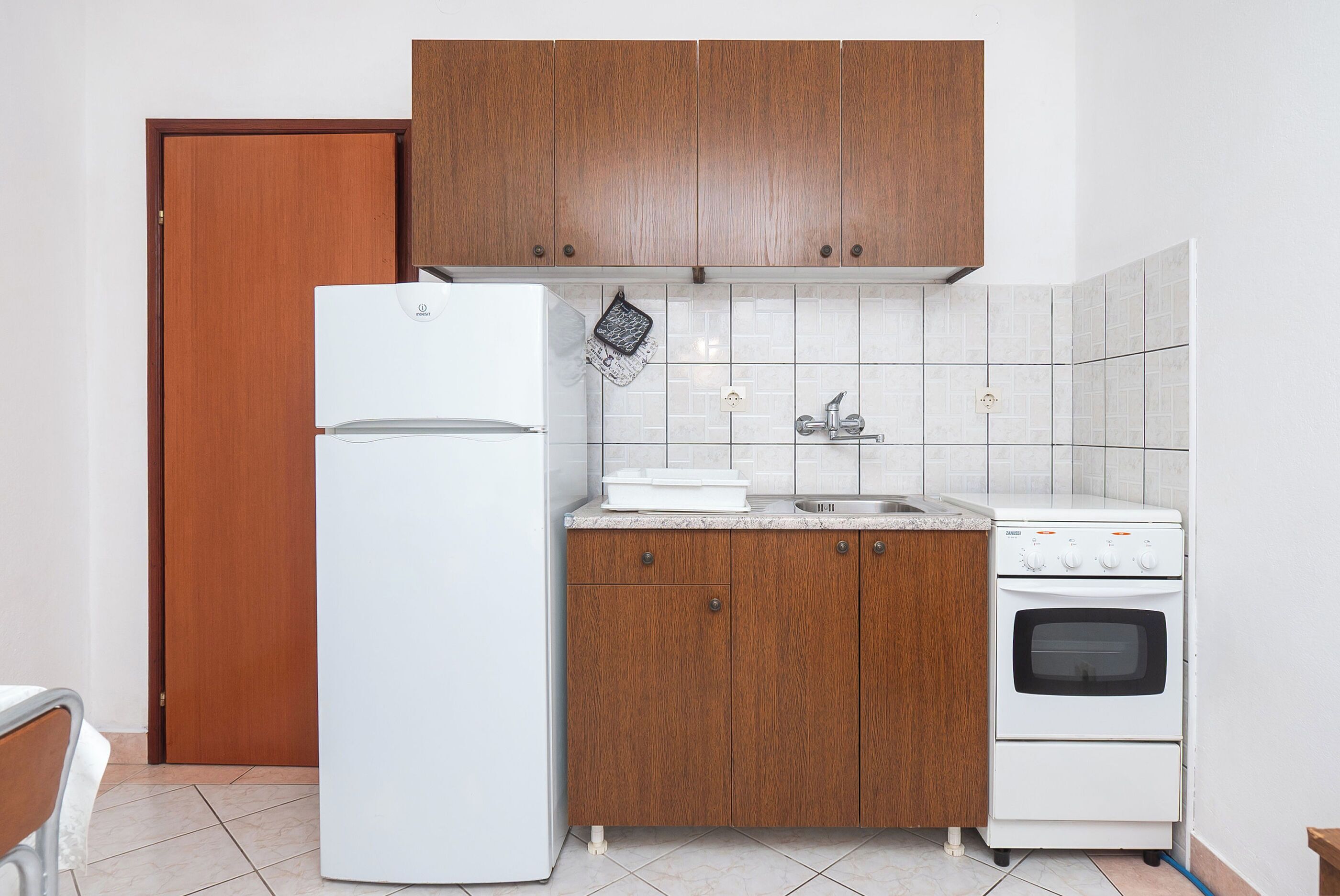 Eine kompakte Küche mit Holzausstattung, einem weißen Kühlschrank, einer Spüle und einem eingebauten Backofen.