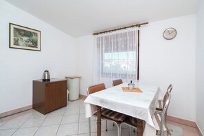 Ein Essbereich mit Tisch, Stühlen, einer Kaffeemaschine, einem Schrank und einem Fenster mit Vorhängen.