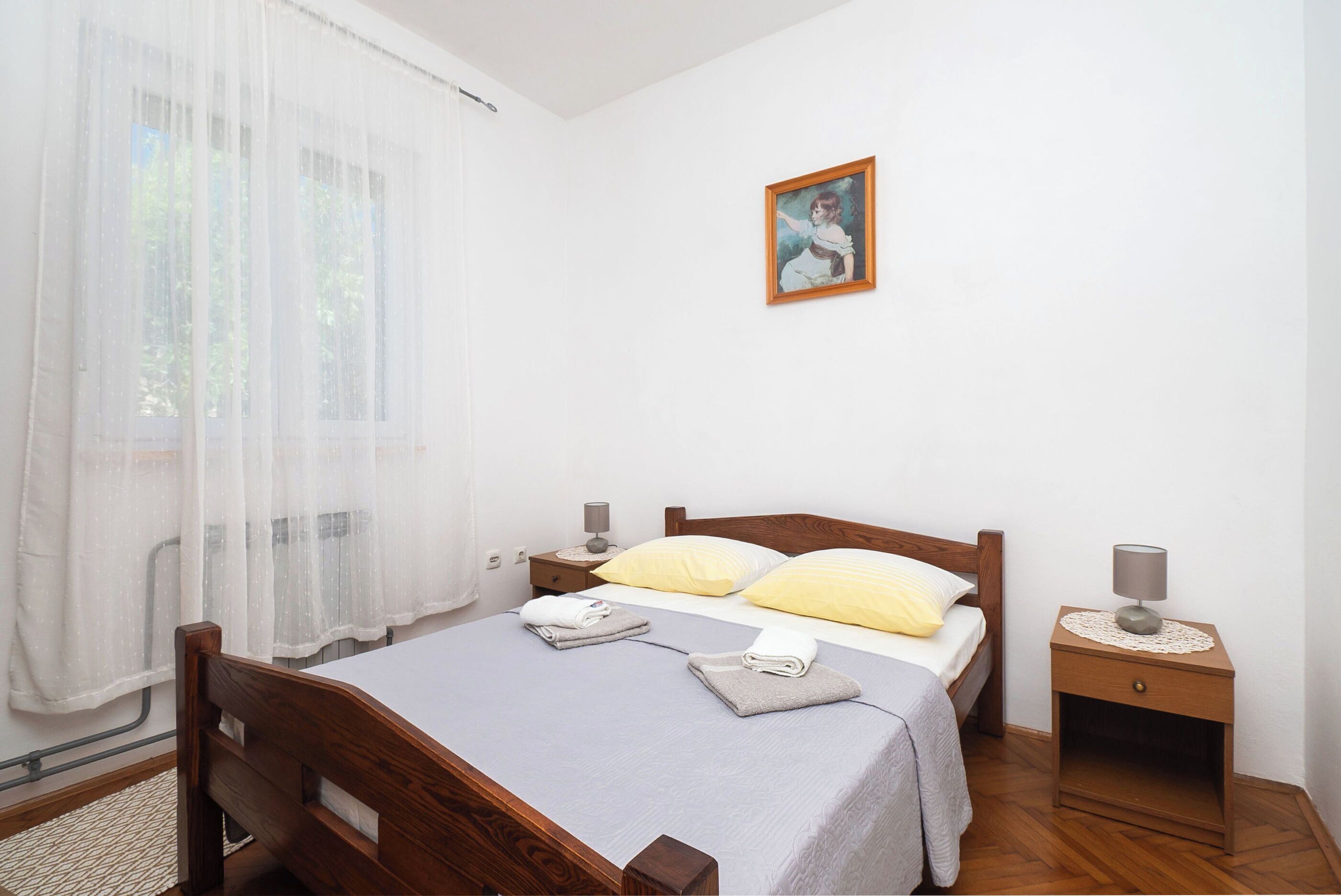 A bedroom with a wooden bed, two bedside tables, a night lamp, and a painting on the wall.