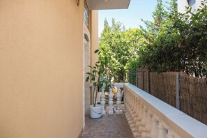 Ein schmaler Außenkorridor mit Steinboden, weißer Balustrade und Kübelpflanzen.