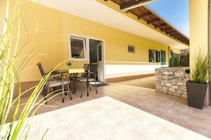 An outdoor patio area with a table and chairs, a stone wall, and a potted plant. - House Violica (Vodice)