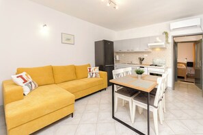 A modern apartment with a yellow sofa, a dining table, and a kitchen area. - House Violica (Vodice)