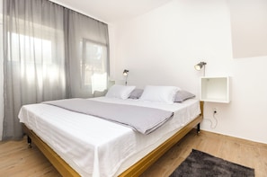 A modern bedroom with a single bed, white bedding, a grey throw, a wooden floor, a grey rug, and two bedside lamps. - House Violica (Vodice)