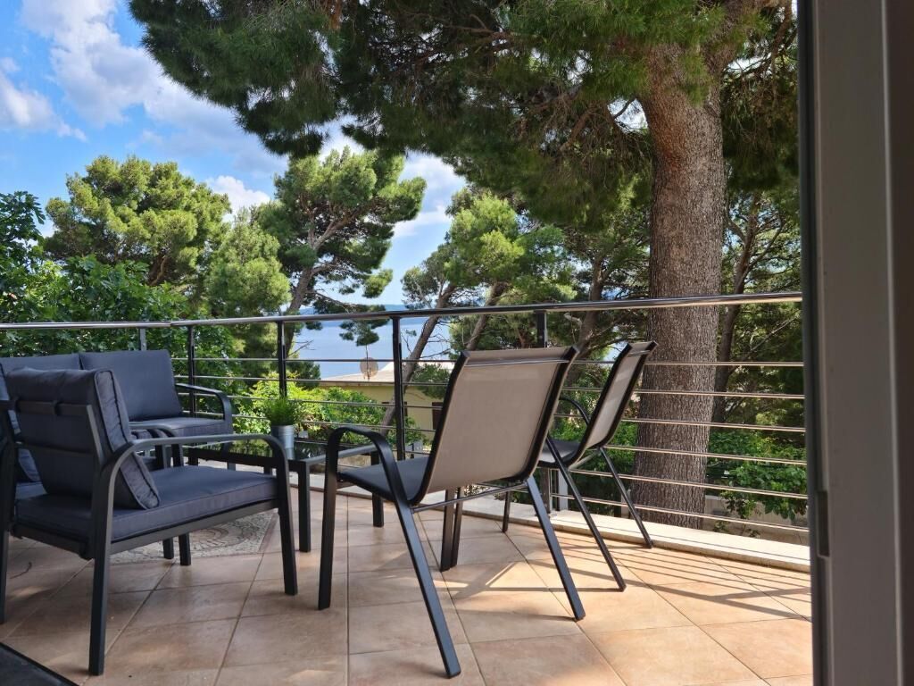 A balcony with two chairs and a sofa, overlooking a body of water and trees.
