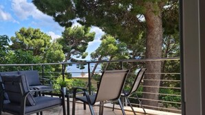A balcony with two chairs and a sofa, overlooking a body of water and trees. - House Pine Tree (Omis)